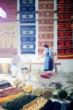 two women are sitting in front of rugs and other items on the floor,