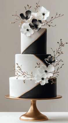 a three tiered cake with black and white flowers on the top is decorated with gold trim