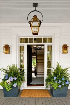 the front entrance to a house with potted plants and a lantern on the porch