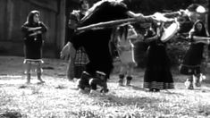 black and white photo of children playing with an elephant in the yard, while adults watch