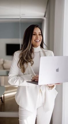 a woman in white is smiling while using her apple laptop and looking at the camera