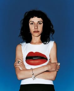 a woman with her arms crossed wearing a white shirt and black skirt, standing in front of a blue background