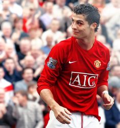 a man in a red shirt is playing soccer with people watching from the sidelines