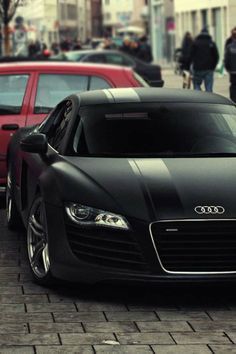 a black car parked on the side of a road next to a red car and people walking by