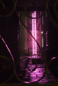 a purple light is shining in an alley way with iron bars on either side and a gate at the end