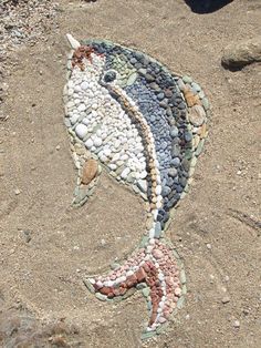 a fish made out of rocks on the sand with pebbles in it's mouth