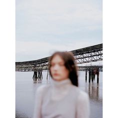 a woman standing in front of the water with a bridge in the back ground behind her