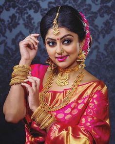 a woman in a red and gold sari with jewelry on her head, posing for the camera