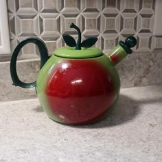 a green and red teapot sitting on top of a counter