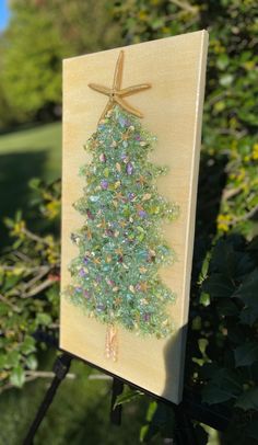 a small wooden christmas tree on a easel in front of some bushes and trees