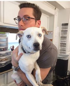 a man holding a white dog in his arms and looking at the camera with blue eyes