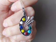 a person holding a silver necklace with paint on it