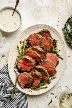 sliced steak on a plate next to two glasses of white wine and some green beans