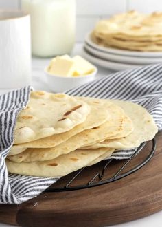 a stack of flatbreads sitting on top of a wooden plate next to a glass of milk