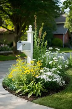 a white mailbox sitting in the middle of a lush green yard next to flowers