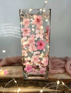 a vase filled with pink flowers sitting on top of a wooden table covered in fairy lights