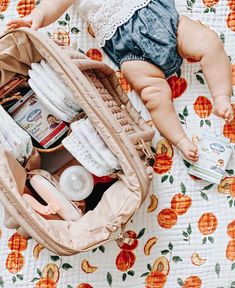 a baby in a diaper is sitting inside an open suitcase on a floral blanket