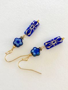 "Stunning deep sapphire blue Czech flower beads with golden bronze details. 20 x 8 mm pressed glass rectangles. Wire wrapped with 10 mm blue Czech glass posies and antique gold bead accents. Gold plated French ear hooks. Total drop 2\"." Blue Rectangular Earrings With Ear Wire, Blue Rectangular Earrings, Nickel Free Blue Rectangular Jewelry, Blue Earrings With Colorful Czech Glass Beads, Blue Czech Glass Beaded Earrings With Dangling Beads, Blue Adjustable Czech Glass Beaded Earrings, Elegant Blue Czech Glass Flower Earrings, Blue Czech Glass Flower Earrings, Sapphire Blue Earrings