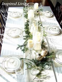 the table is set for christmas dinner with white plates and silverware, greenery and candles