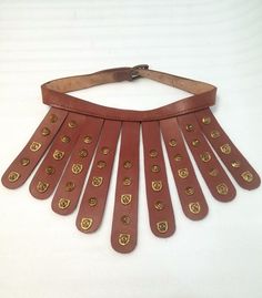 a brown leather necklace with gold embellishments is displayed on a white surface