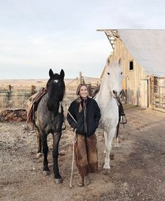 a woman standing next to two horses in front of a barn