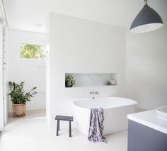 a white bath tub sitting in a bathroom next to a sink and window with potted plants on it