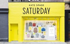 a yellow storefront with clothes on display in front of the building that says kate spade saturday