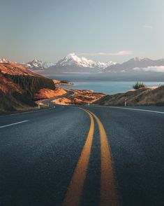 an empty road in the middle of nowhere with mountains in the background and snow capped peaks