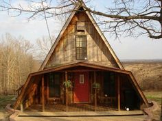 a small wooden house with a red door and windows on the front porch, surrounded by trees