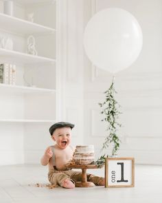 a baby boy sitting on the floor with his first birthday cake in front of him