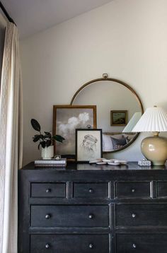 a dresser with a mirror, lamp and pictures on it