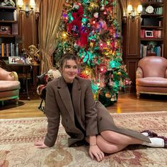 a woman sitting on the floor in front of a christmas tree