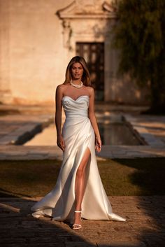 a woman in a white dress is posing for the camera with her leg slit down