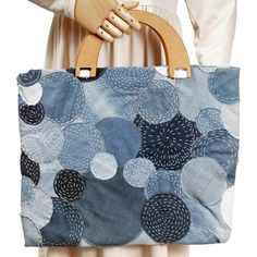 a woman holding a blue and white bag with circular designs on the front, while wearing a beige dress