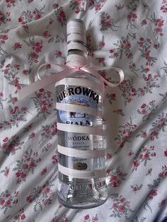 a bottle of vodka sitting on top of a bed next to a flowery blanket