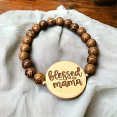 "Blessed Mama Wood Bead Engraved Bracelet  This beautiful bracelet is made from wood beads and features an engraved 1.5inch flat round. Engraving \"Blessed Mama\" makes the perfect gift for Mother's Day, Mom's Birthday, birth of a child, Valentine's Day, or just to celebrate Mom.  Bracelet is made from durable elastic cord and securely tied. Comfortably fits 7inch wrist with plenty of stretch to accommodate a variety of sizes. If you need a specific size a new bracelet can be made for you from available stock, please message me to discuss details. Each bracelet will vary slightly due to variations in wood and engraving. If you would like to preview the available bracelets and select a specific one please message me before purchasing." Wooden Beaded Bracelets As Gift, Wooden Beaded Bracelets Perfect For Gifts, Wooden Bracelets With Round Beads For Gifts, Wooden Beaded Bracelets For Gifts, Adjustable Wood Bracelets As Gifts, Natural Wood Beaded Bracelets As Gift, Natural Wood Beaded Bracelets For Gifts, Adjustable Wooden Bracelets As Gifts, Natural Wood Beaded Bracelet As Gift