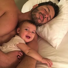 a man laying in bed next to a baby with his arm around the head of another man