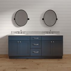 two round mirrors on the wall above double sinks in a white and blue bathroom with wood flooring