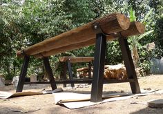 a wooden bench sitting on top of a dirt ground next to some trees and logs