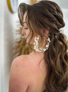 a woman with long brown hair wearing large white flowers in her hair is looking down at the ground