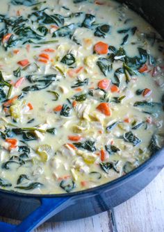 a blue pot filled with cheese and vegetables on top of a wooden table next to a spoon