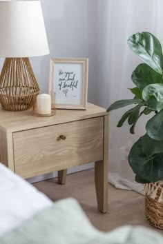 a wooden table with a lamp and a plant on it next to a white bed