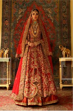 a woman in a red and gold bridal gown standing next to a wall with an ornate