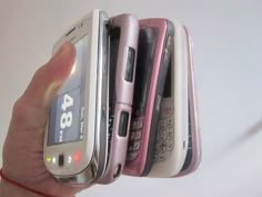 a person holding four different cell phones in their hands, one is pink and the other is white