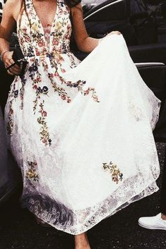 a woman in a white dress standing next to a car and holding onto her skirt