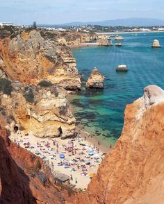 the beach is crowded with people and umbrellas in the water next to rocky cliffs