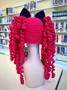 a pink crocheted hat with black ears on top of a white mannequin