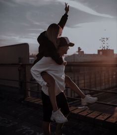 a man and woman standing on top of a roof with their arms in the air