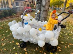 a little boy in a costume riding on a wagon filled with balloons