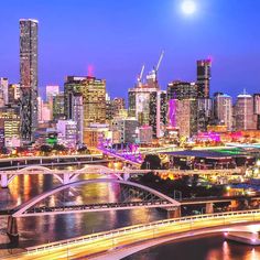 the city skyline is lit up at night, with lights on and bridge in foreground